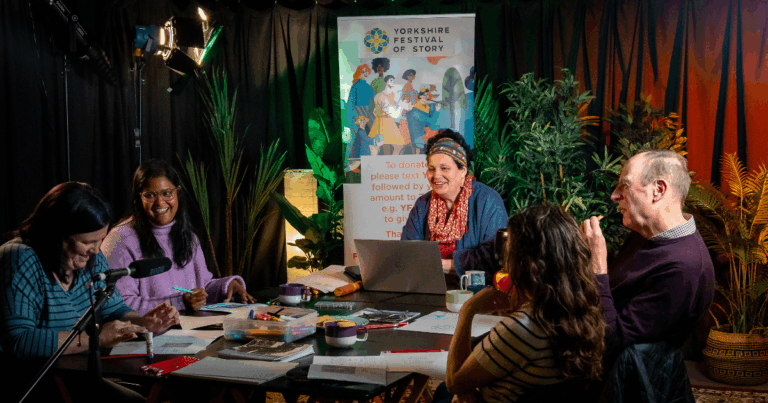How to Find and Tell Your Story - people sit around a table as Sita leads a workshop, smiling and laughing.