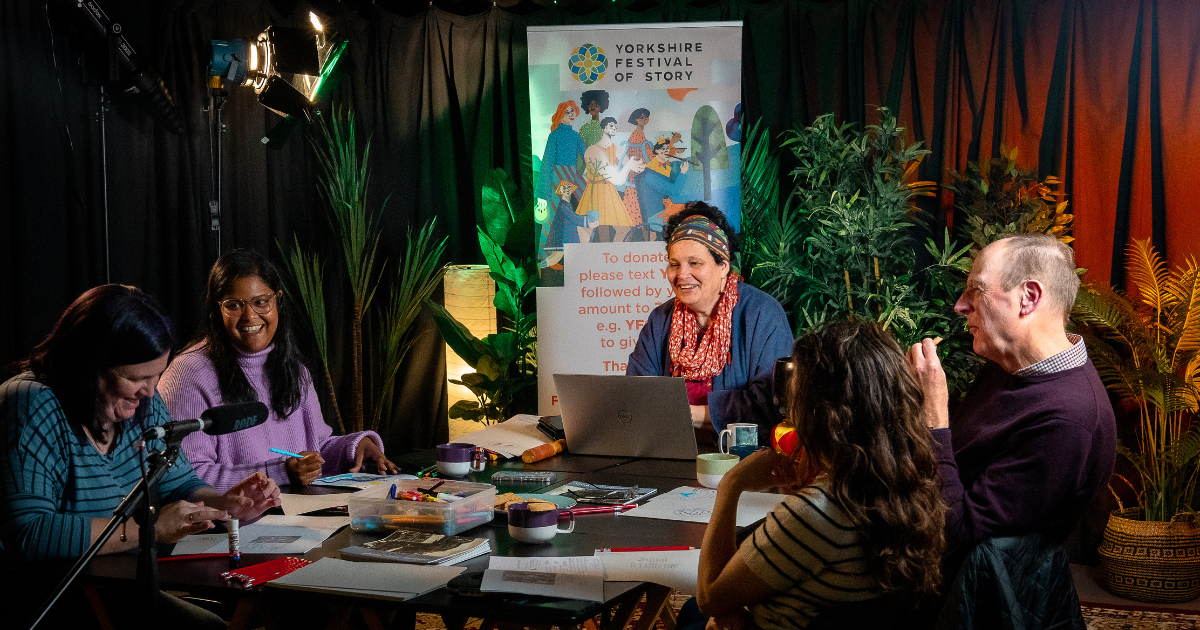 How to Find and Tell Your Story - people sit around a table as Sita leads a workshop, smiling and laughing.