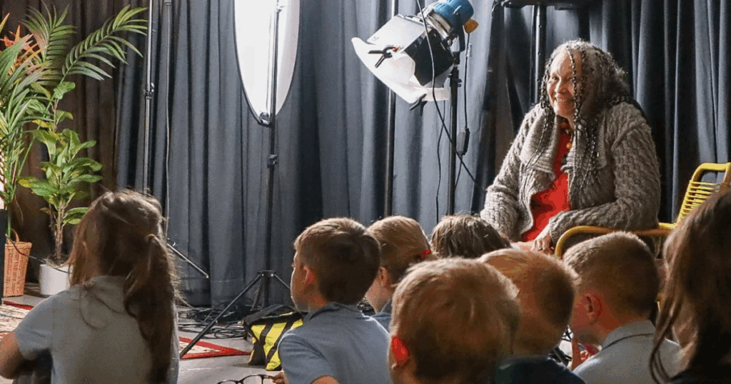 Storytelling framework for teachers - Sita Brand smiles cheekily at the camera whilst schoolchildren sat around her watch a storyteller