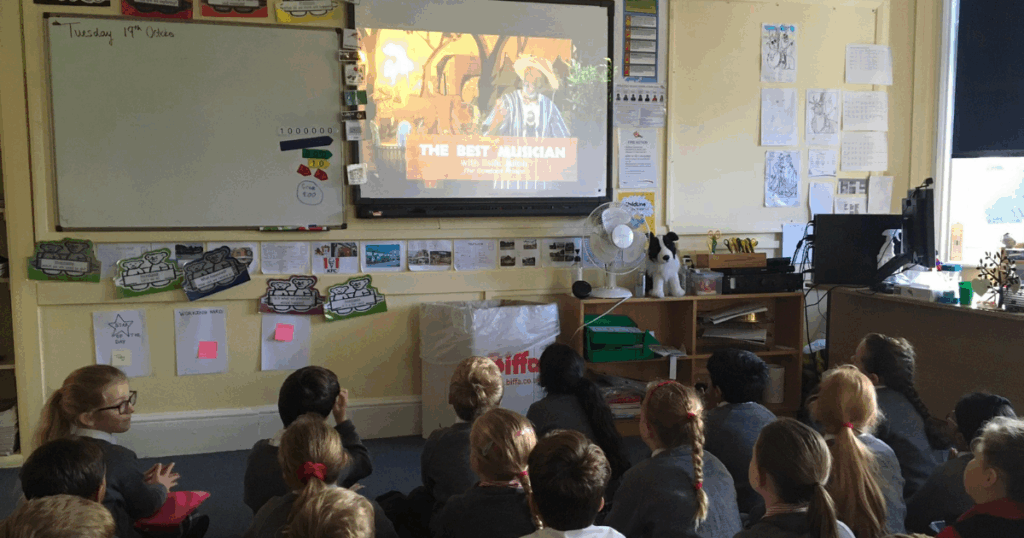 Free classroom story resource - children watch a screen with a live storytelling performance being streamed.