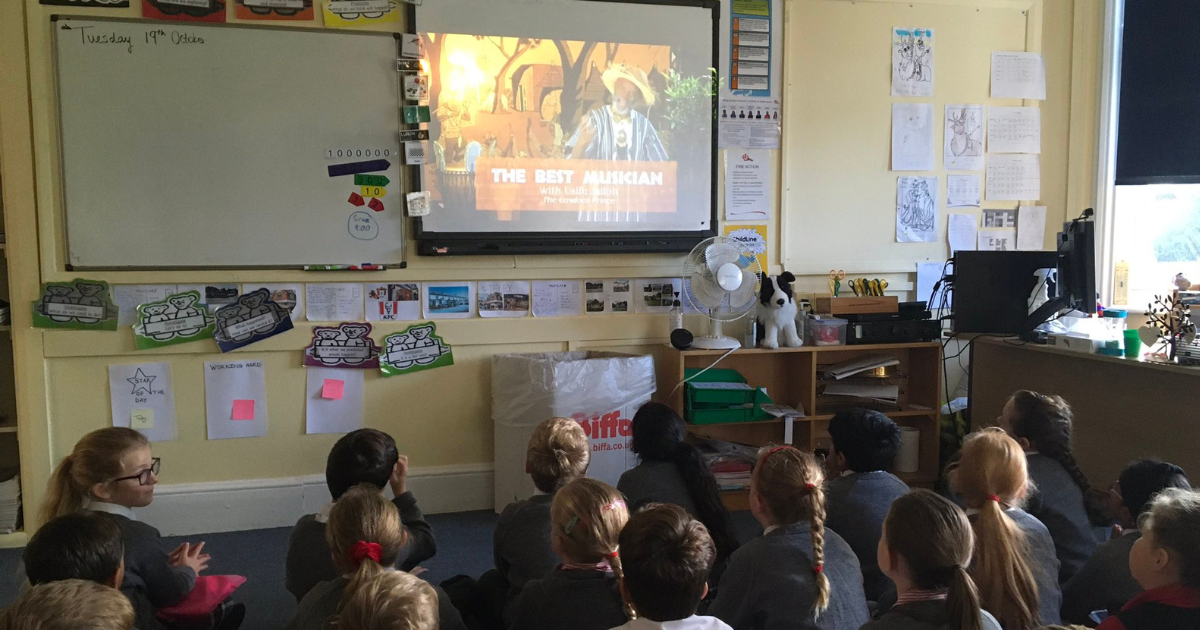Free classroom story resource - children watch a screen with a live storytelling performance being streamed.